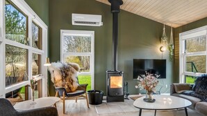 Un salon chaleureux avec une cheminée, des sièges confortables et de grandes fenêtres donnant sur l’extérieur.