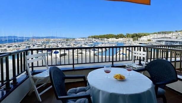 A balcony with a table and chairs, overlooking a marina with boats and a clear blue sky. - Feel the sea breeze from your balcony overlooking the port. (l'Escala)