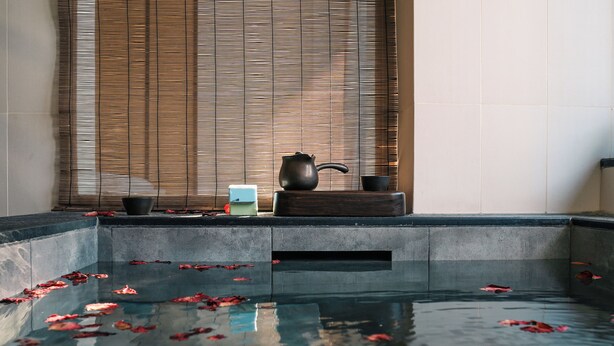 A tranquil indoor pool with floating rose petals, a teapot, and a cup on a wooden ledge. - BEIJING DASEIN HOTEL (Beijing)