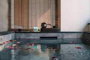 A tranquil indoor pool with floating rose petals, a teapot, and a cup on a wooden ledge. - BEIJING DASEIN HOTEL (Beijing)