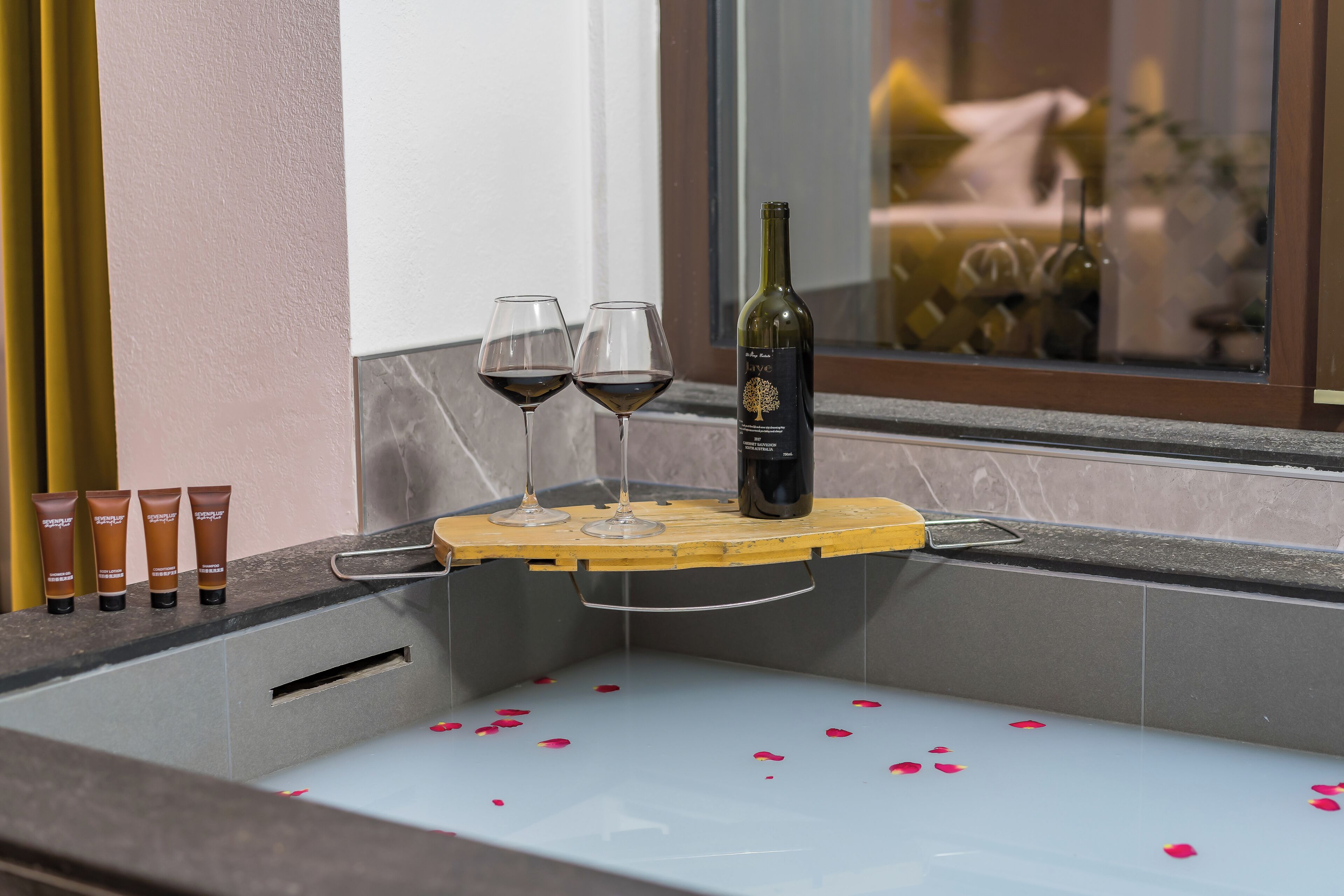 A bathtub with rose petals, two wine glasses, and a bottle of wine.