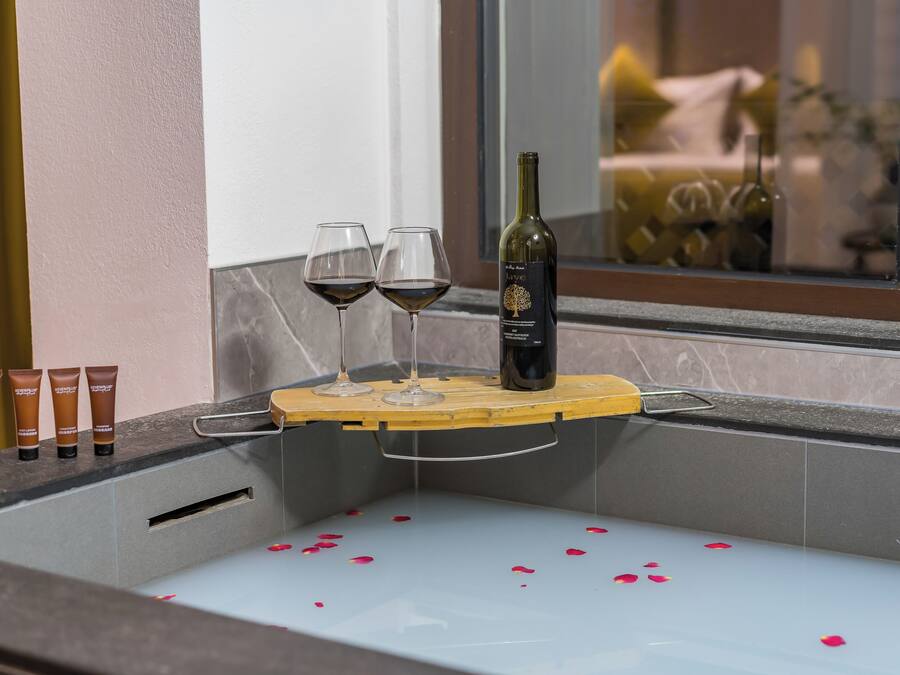 A bathtub with rose petals, two wine glasses, and a bottle of wine.