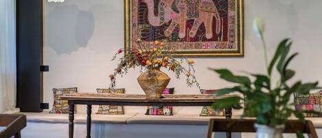 A dining area with a wooden table, a vase with flowers, and a colorful elephant tapestry on the wall.