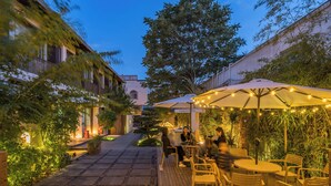 A wooden deck with outdoor seating and string lights, surrounded by greenery and buildings. - BEIJING DASEIN HOTEL (Beijing)
