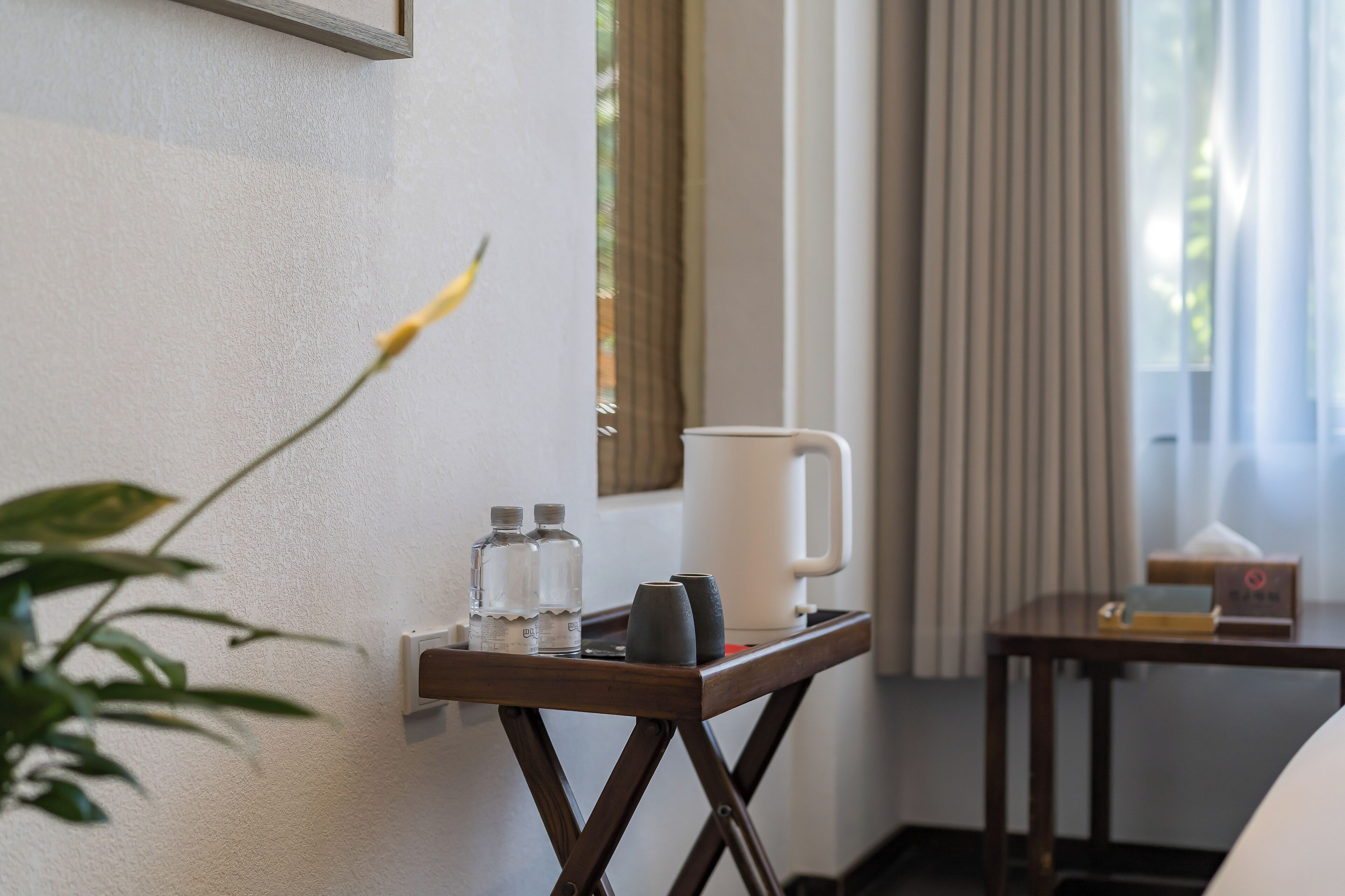 A hotel room with a bedside table holding a water bottle, a mug, and a tissue box.