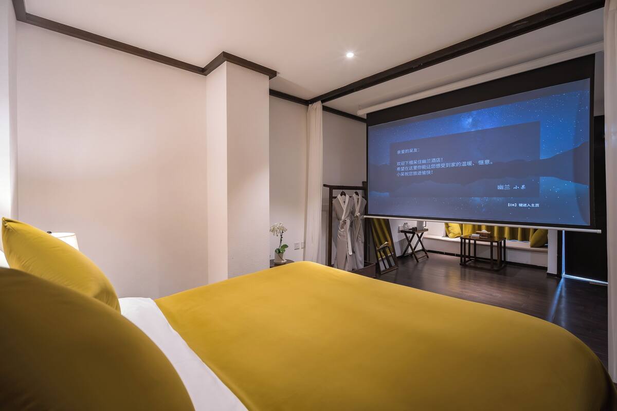 Une chambre d’hôtel équipée d’un lit, d’un écran de projection, d’une petite table et d’une chaise.