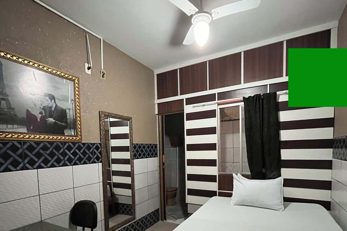 Une chambre d’hôtel avec un lit, un bureau, une chaise, un ventilateur de plafond et une porte de salle de bain.