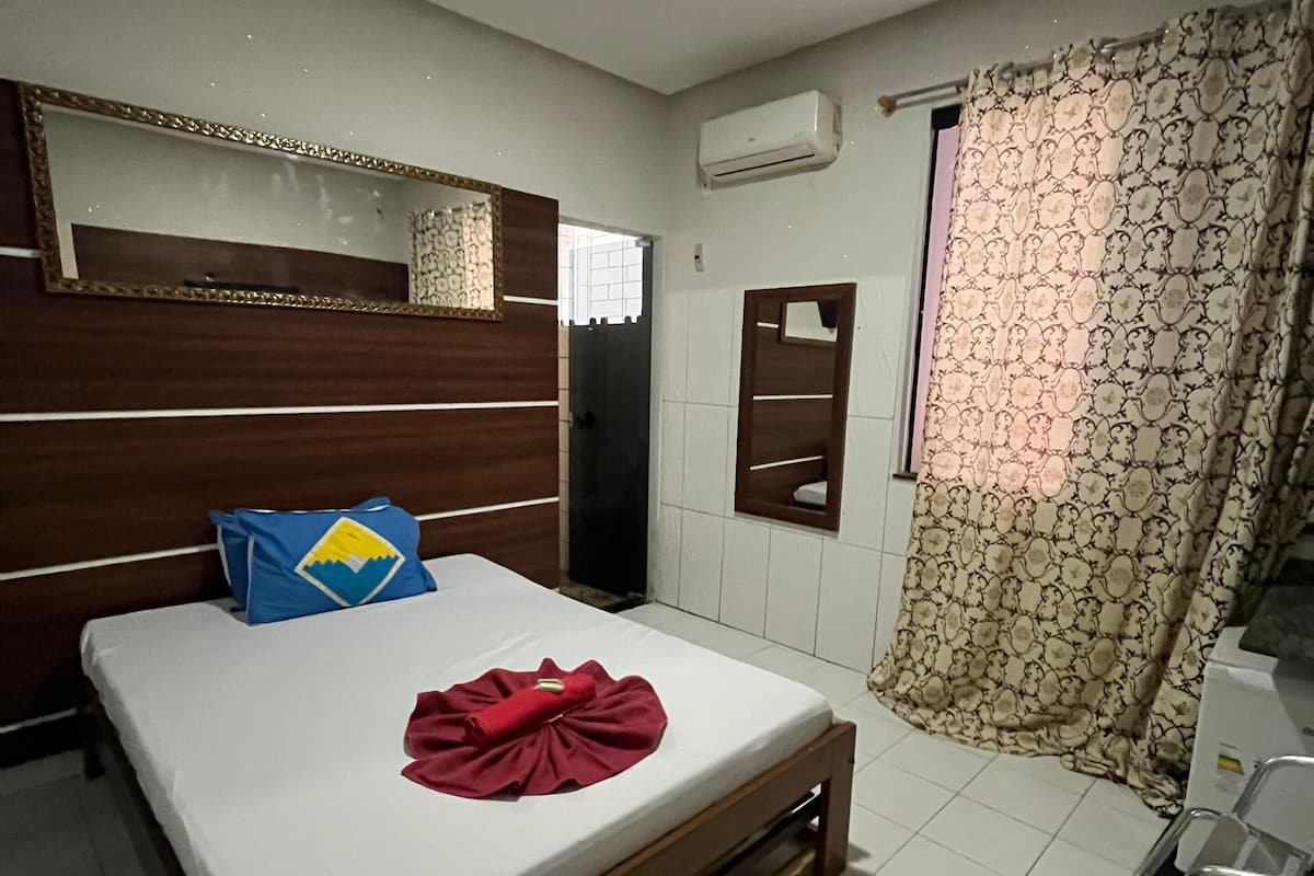 Une chambre d’hôtel comprenant un lit, une table de chevet, un miroir, une armoire, un appareil de climatisation et un rideau.