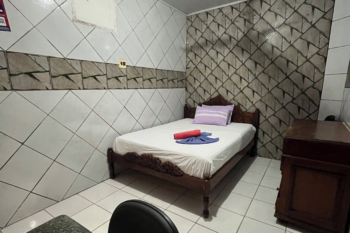 Une chambre avec un lit, un bureau et une chaise. Il y a un ventilateur de plafond et un climatiseur fixé au mur.