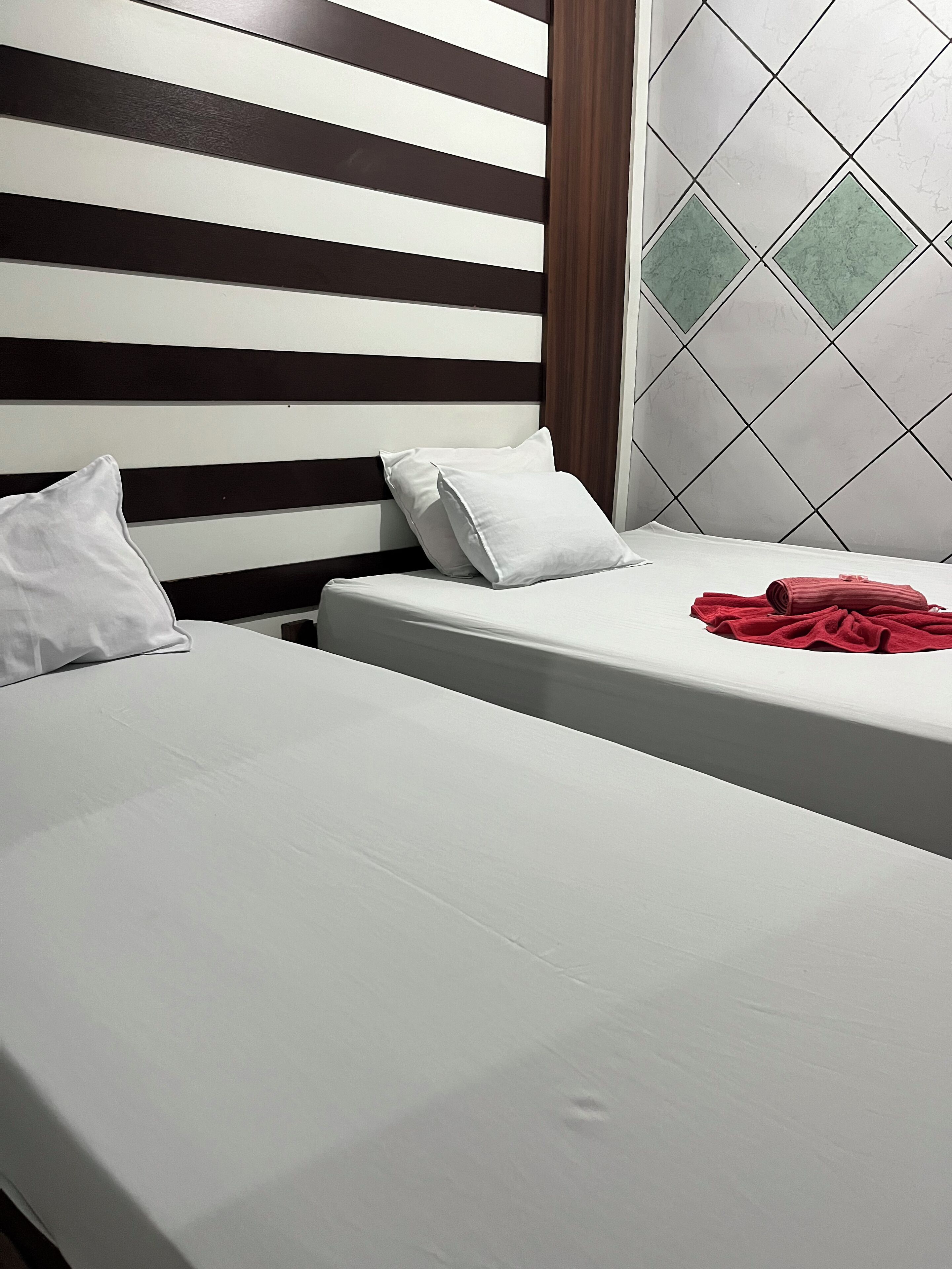 Quarto de hotel com duas camas, cabeceira listrada e parede revestida em azulejos.