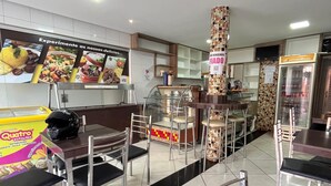 Interior de un restaurante con un mostrador central de servicio, varias mesas y sillas, y un suelo de baldosas.