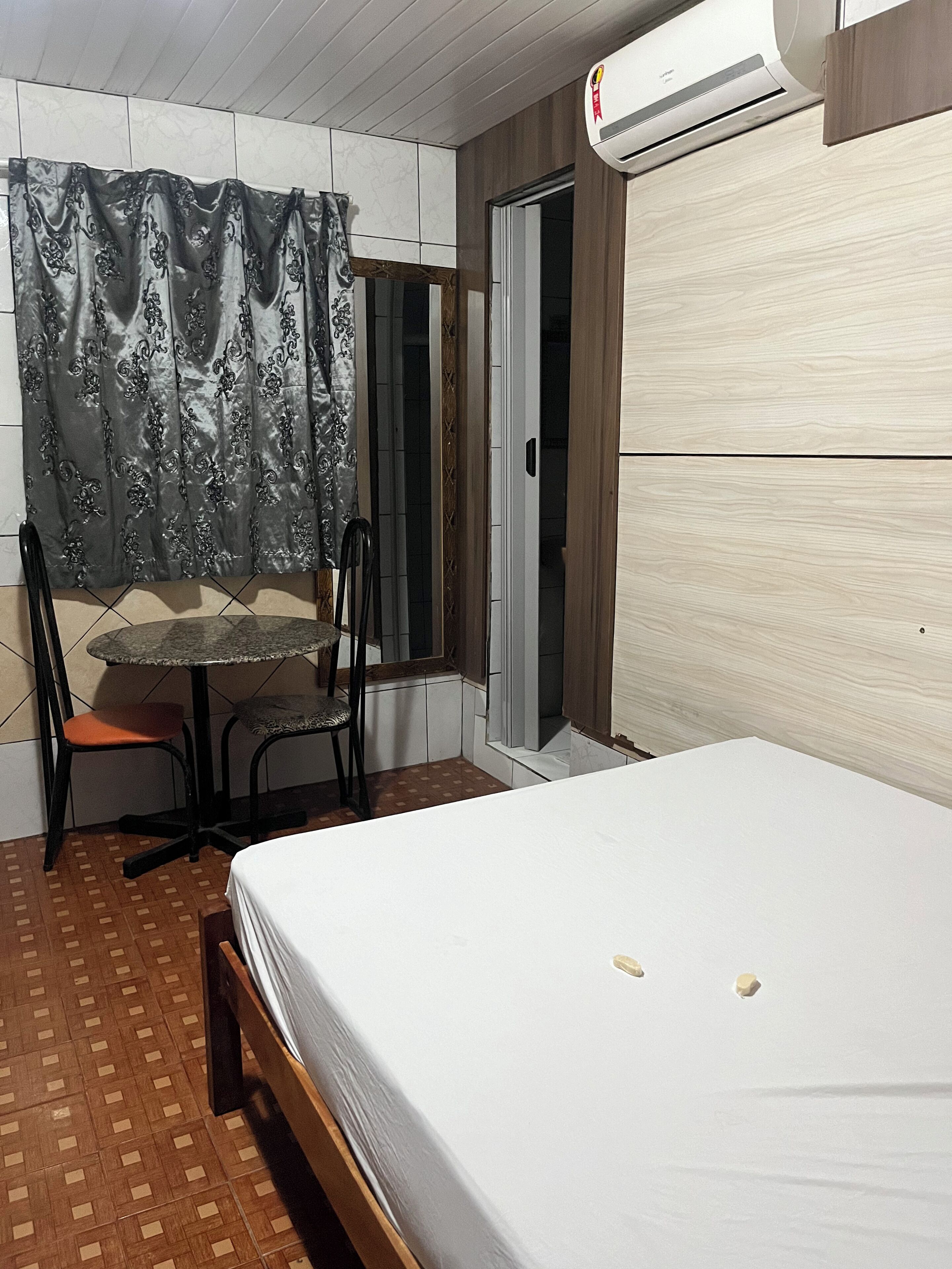 A bedroom with a bed, a chair, a table, and an air conditioning unit.