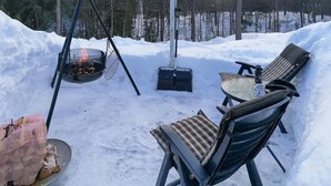 Un espacio al aire libre cubierto de nieve con un pozo de fuego, sillas y una mesa.