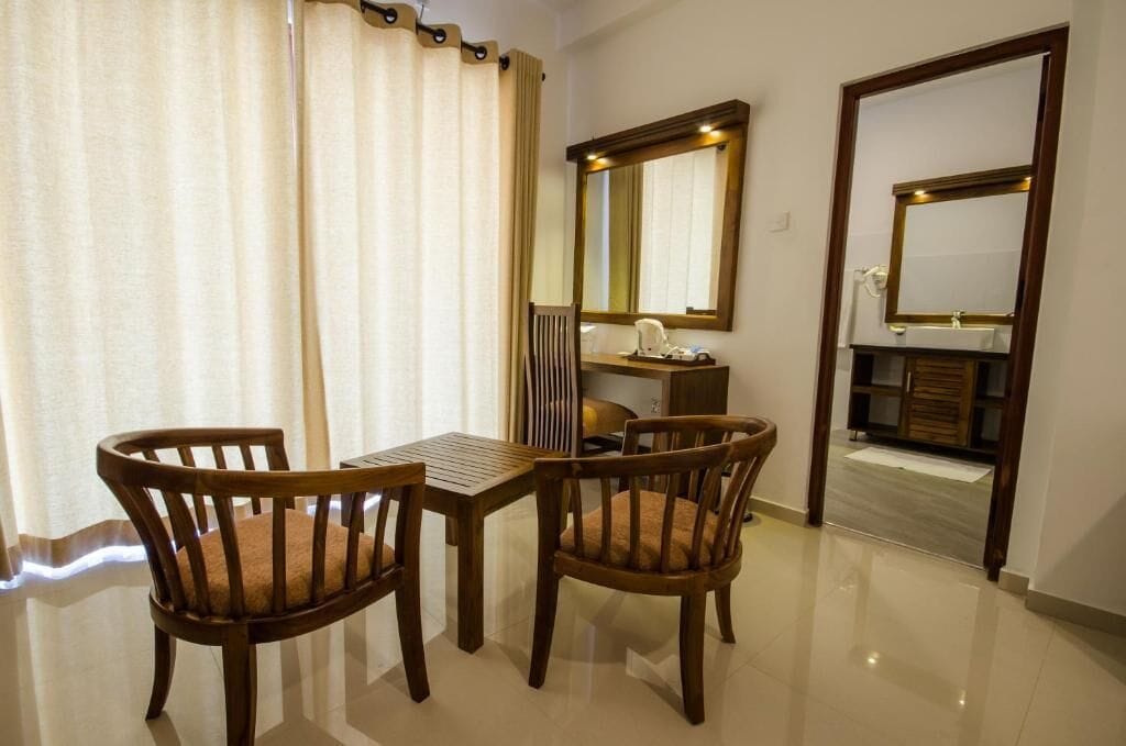 Una habitación de hotel con una mesa de madera y sillas, un espejo grande y un tocador con espejo.