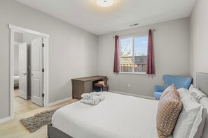 A bedroom with a bed, a desk, a chair, and a window with curtains.