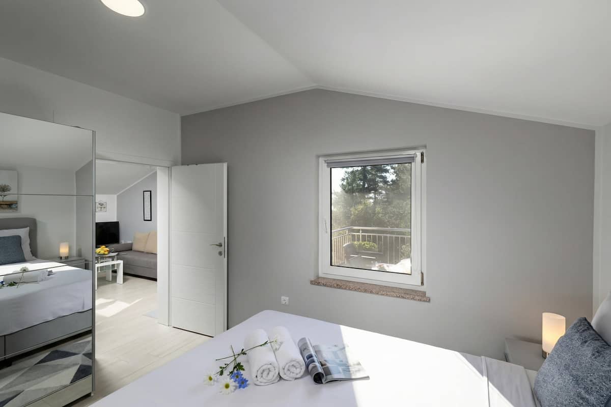 A modern bedroom with a bed, a bedside table, a window, and a mirror.