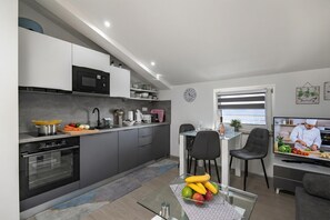A modern kitchen with built-in appliances, a dining area with a TV, and a view to the outside.