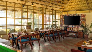 A spacious room with large windows, wooden furniture, and a television on the wall. - Banana Hostel (Pushkar)