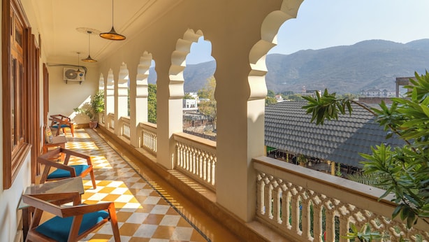 A balcony with a checkered floor, wooden chairs, and a view of mountains. - Banana Hostel (Pushkar)