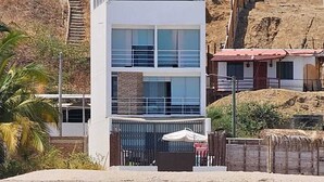 Ein Anwesen direkt am Strand mit einem zweistöckigen Gebäude, einer umzäunten Terrasse und Blick aufs Meer.
