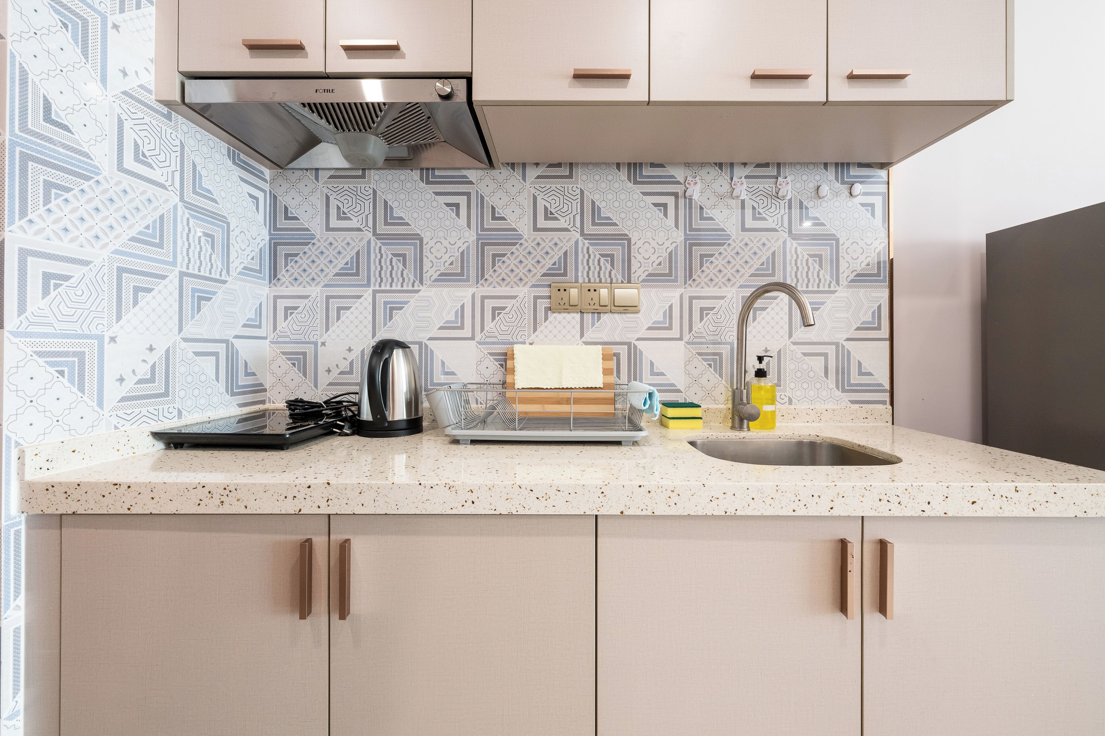 A kitchen with a speckled countertop, a stainless steel sink, and a patterned backsplash.