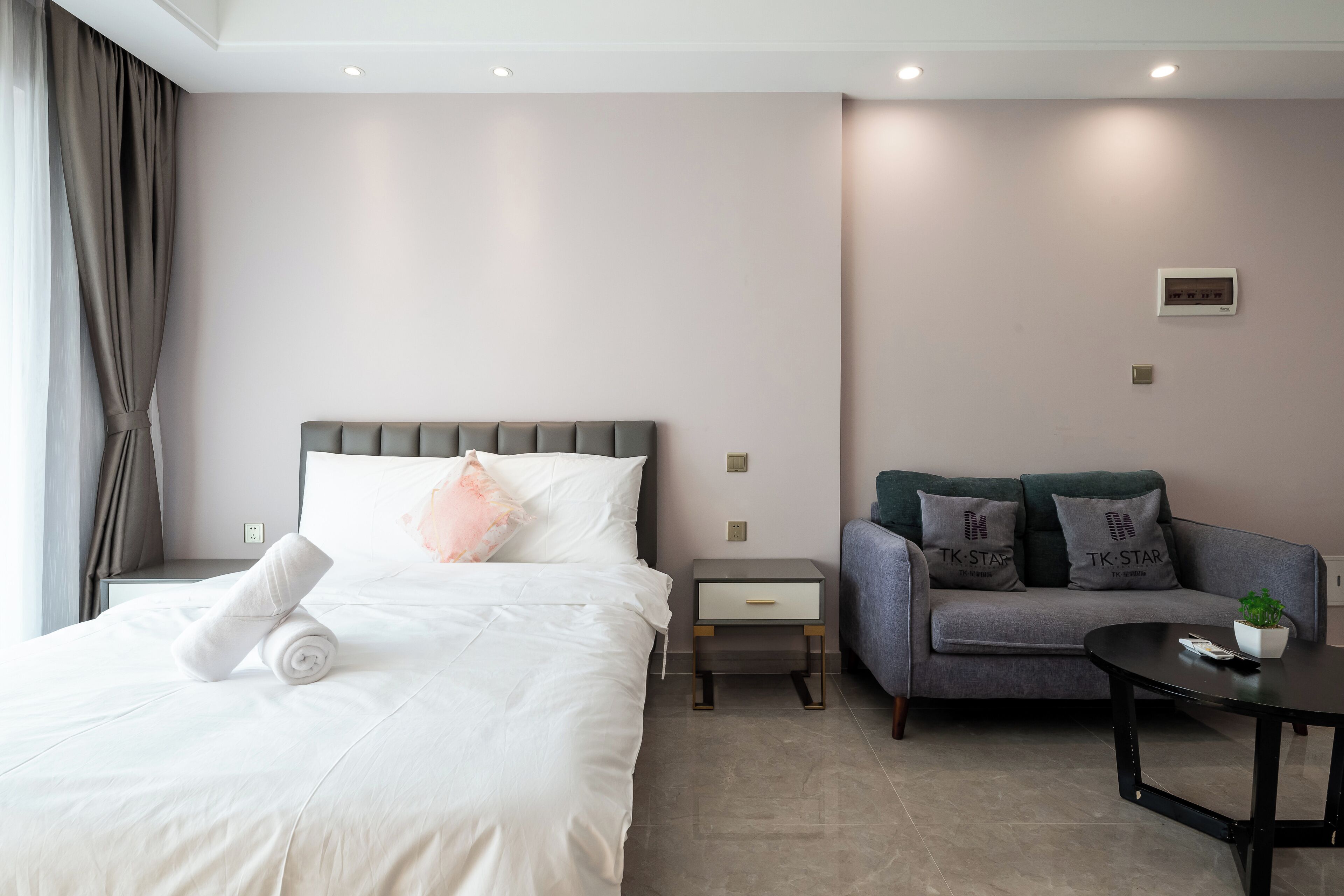A hotel room with a bed, a sofa, a small table, and a potted plant.
