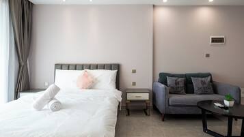 A hotel room with a bed, a sofa, a small table, and a potted plant.