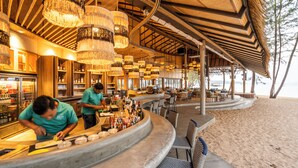 A beachfront bar with a curved counter, hanging chandeliers, and outdoor seating. - JATI Koh Russey (Prey Nob)