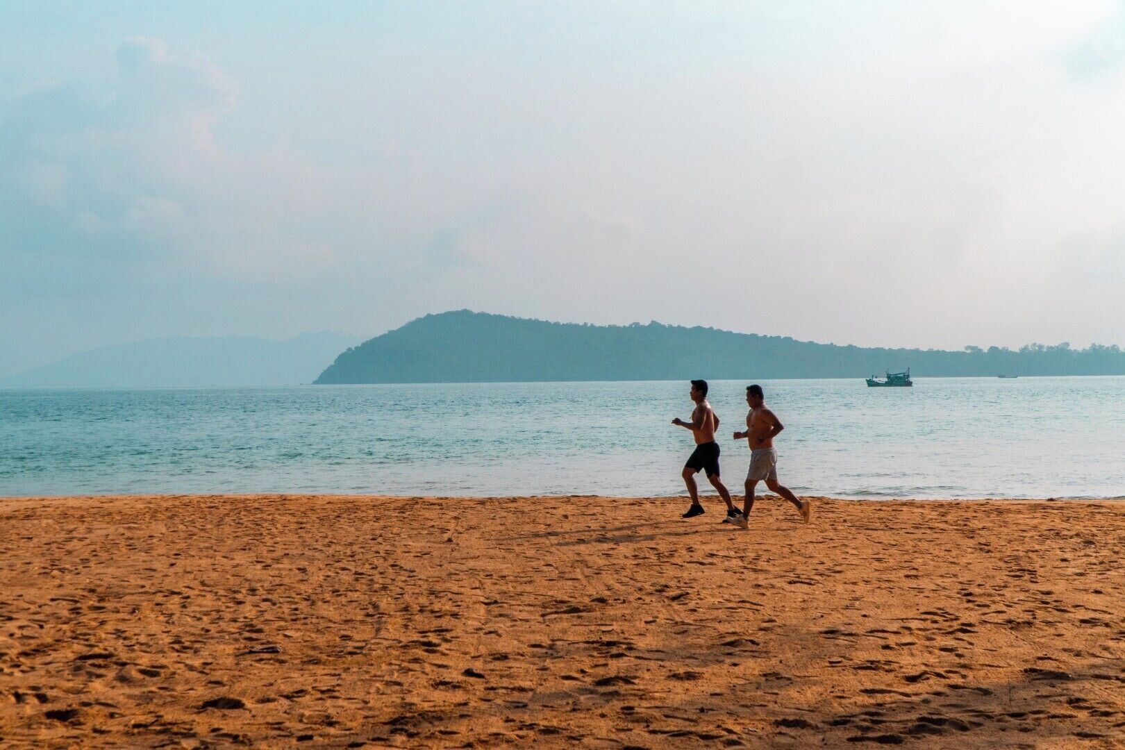 Two people running on a sandy beach with a calm sea and a distant island.