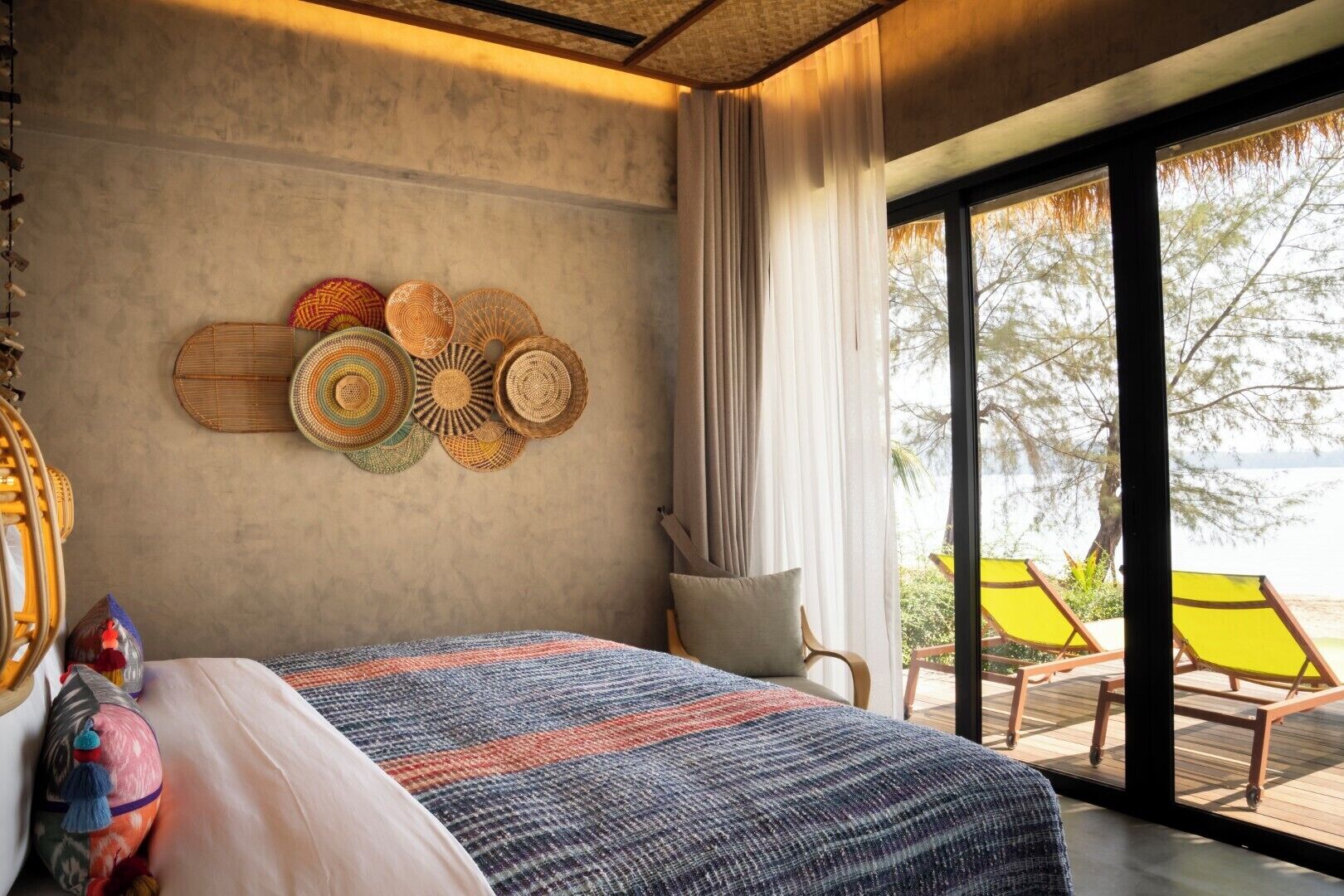 Een slaapkamer met een groot bed, uitzicht op het strand en een wand versierd met gevlochten manden.