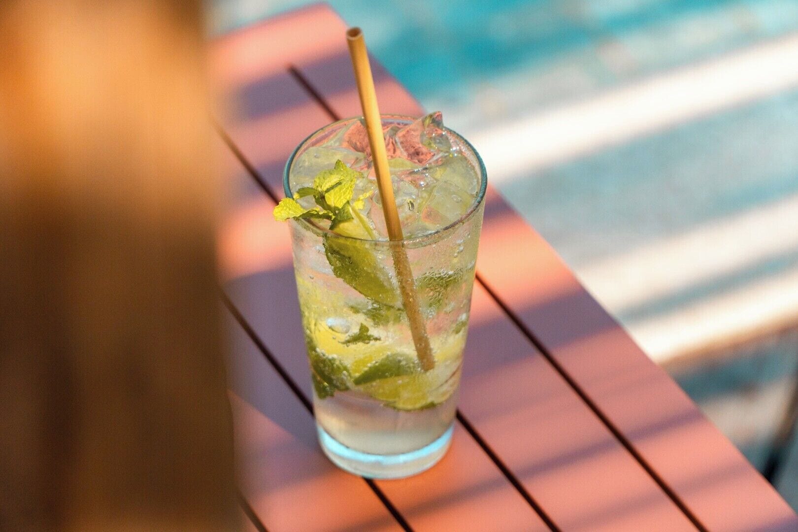 A glass of iced drink with mint leaves and a straw on a wooden table.