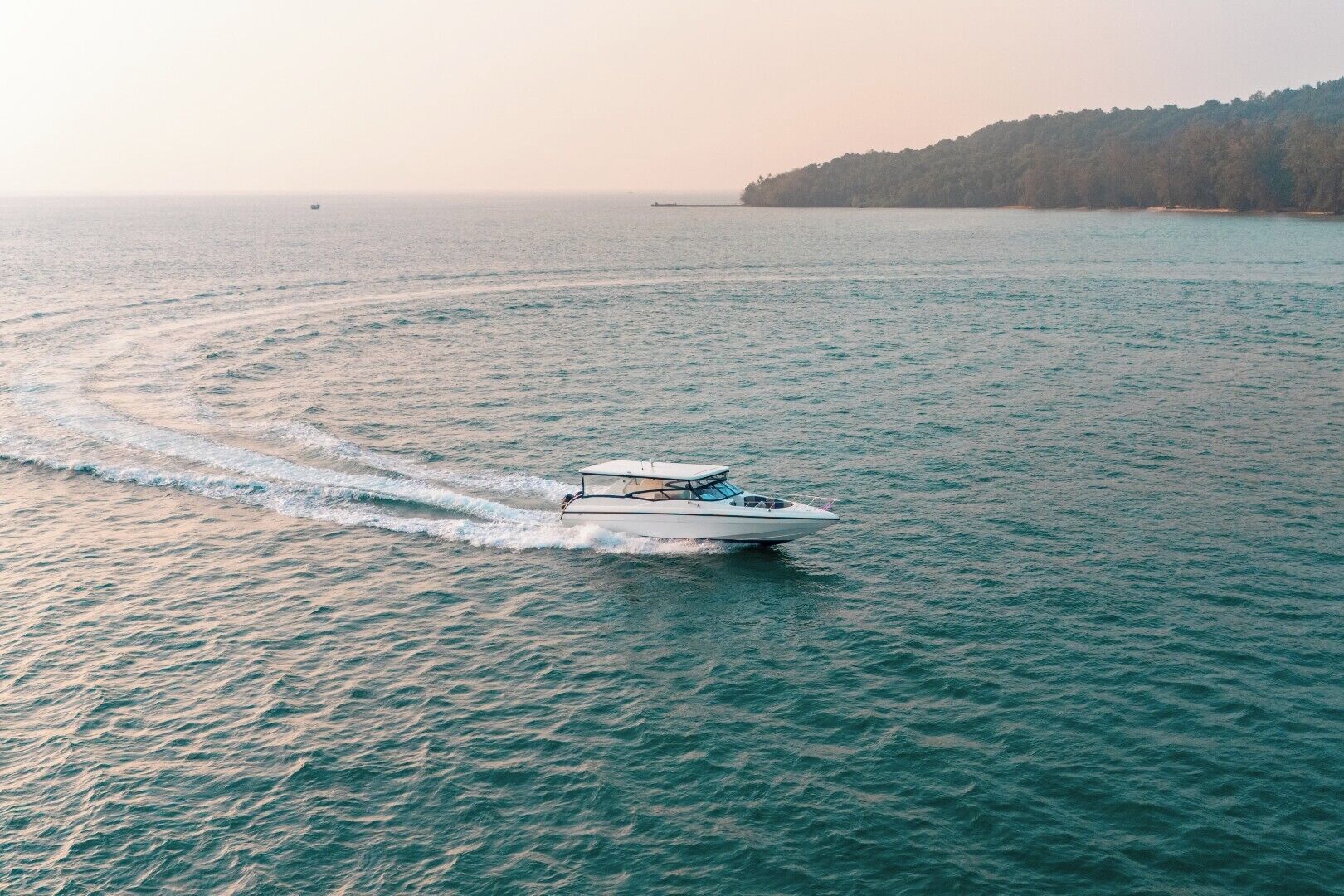 A boat moving across a calm sea with a forested island in the background.