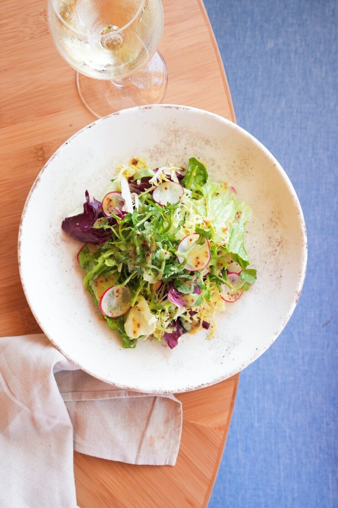 A bowl of mixed greens salad with radishes, served on a white plate.