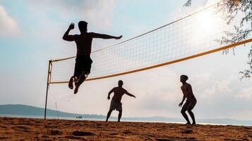 A beach volleyball game with players in shorts and no shirts, a volleyball net, and a clear sky.