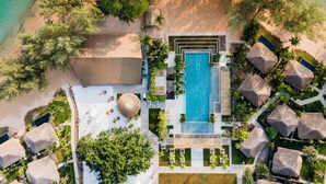 An aerial view of a resort with a central swimming pool, beachfront, and thatched-roof structures. - JATI Koh Russey (Prey Nob)