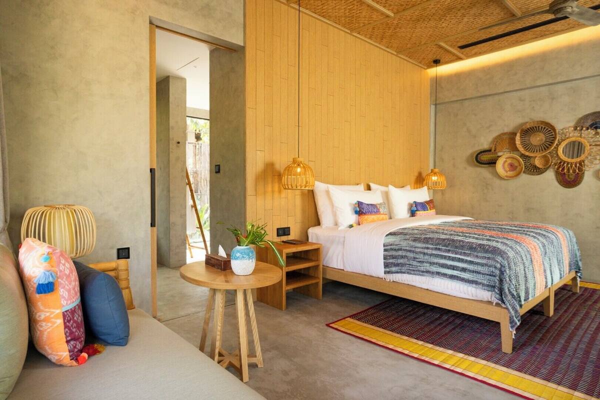 Um quarto moderno com uma cama de madeira, uma mesinha redonda com uma planta e um tapete colorido.