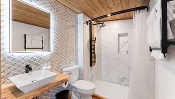A modern bathroom with a wooden vanity, a white toilet, a shower with a black handle, and a tiled wall.
