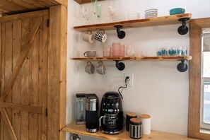 Uma cozinha com prateleiras de madeira que exibem copos e canecas, uma cafeteira e uma chaleira.