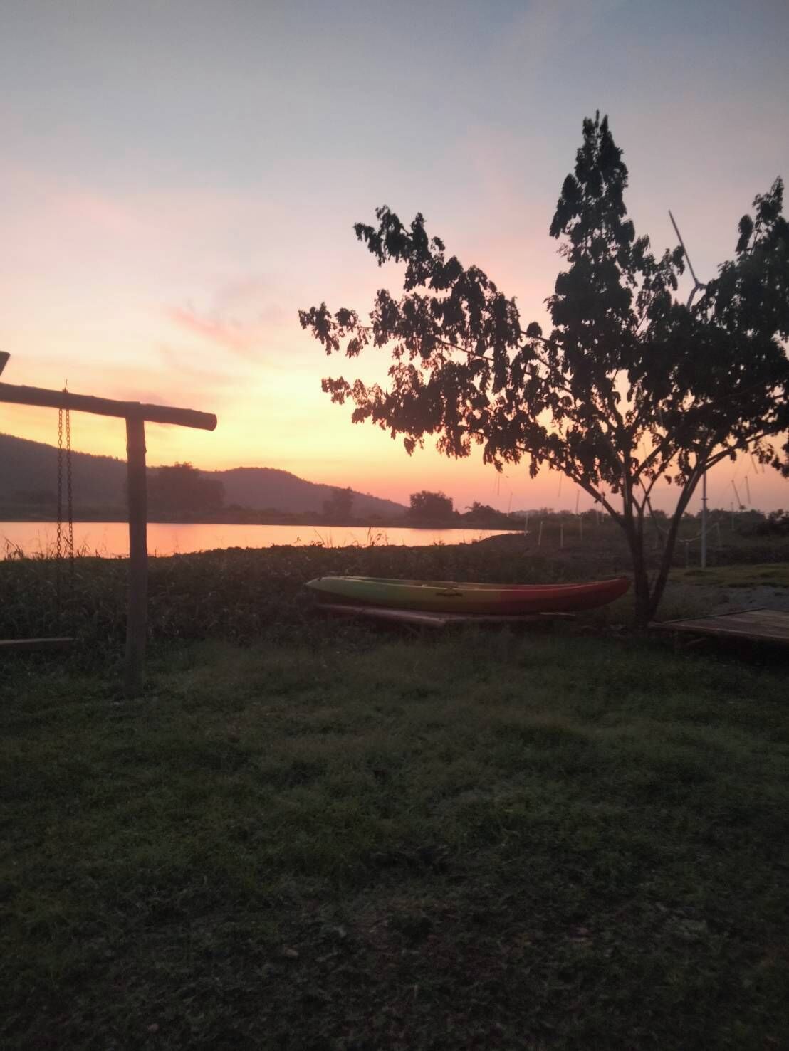 Un cadre extérieur paisible, avec un arbre, une balançoire et des kayaks près d’une étendue d’eau, au coucher du soleil.