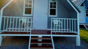 Une maison à deux étages avec une porte d’entrée blanche, deux fenêtres et un porche doté de balustrades et de chaises blanches.