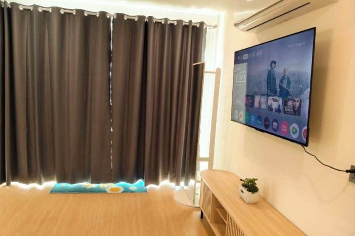 Una habitación con una televisión de pantalla plana grande montada en la pared, un banco de madera y una pequeña planta en maceta.
