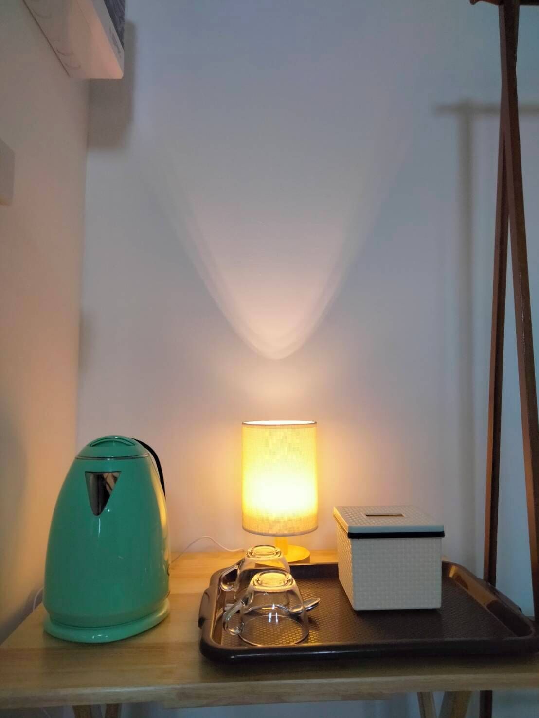 A room with a teal kettle, a tray with glasses, and a lit lamp on a wooden table.
