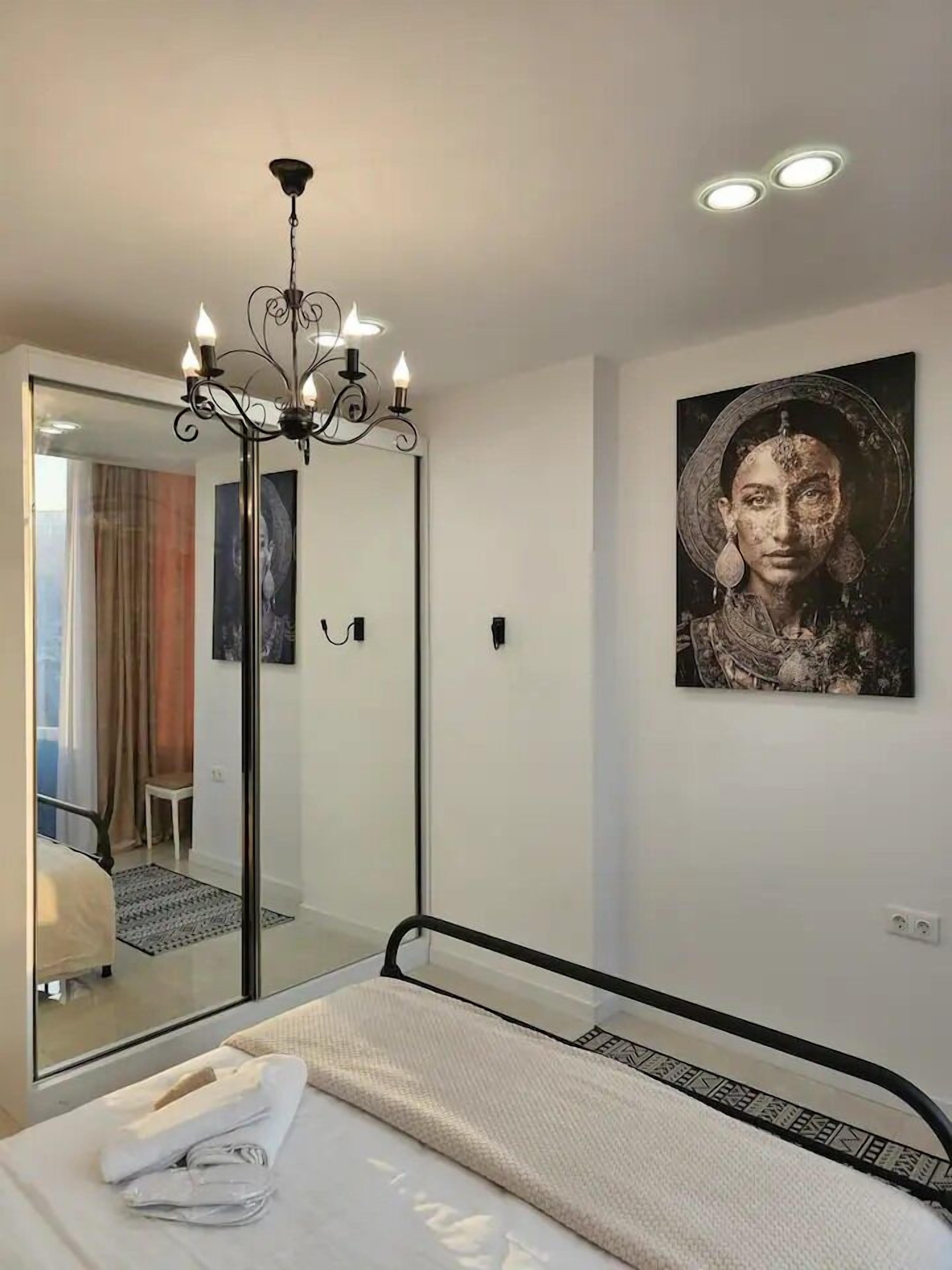 Une chambre à coucher avec un lit, un miroir, un lustre et un tableau au mur.