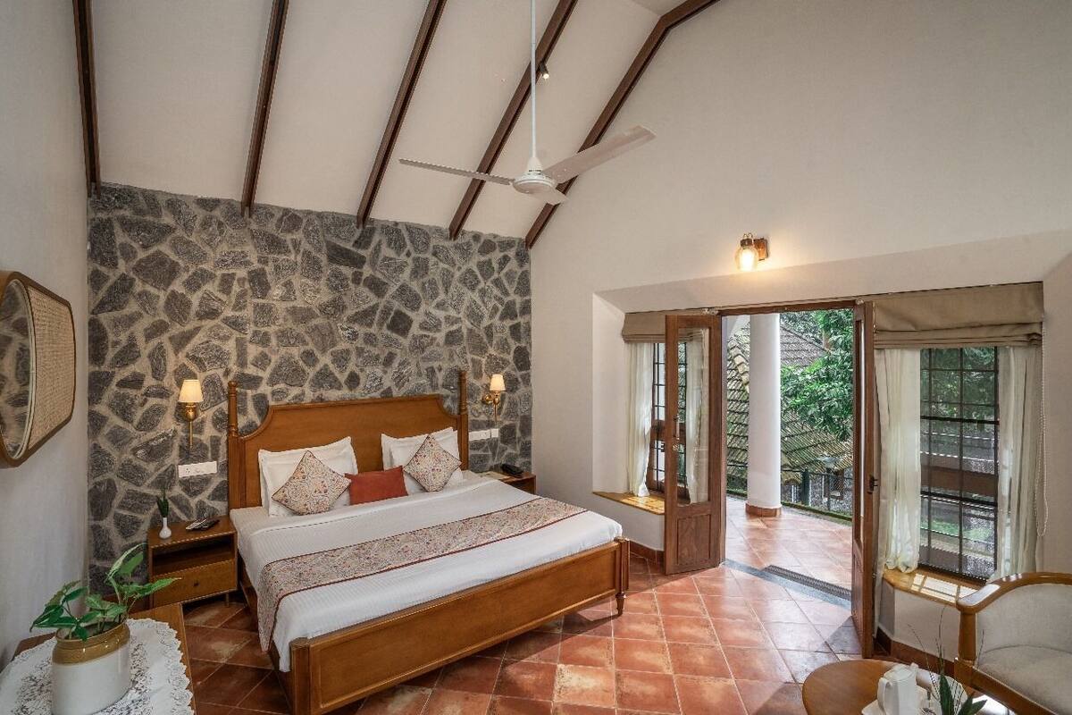 A bedroom with a stone wall, a wooden bed, a ceiling fan, and a view of the outdoors.