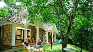 A stone house with a tiled roof, a porch with chairs, and a hammock. - HOTEL TREETOP (Peermade)