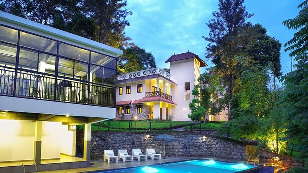 A modern house with a swimming pool, a glass conservatory, and a stone wall. - HOTEL TREETOP (Peermade)