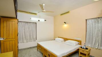 Un dormitorio con una cama individual, un armario de madera, una mesita de noche, un ventilador de techo y una lámpara fijada a la pared.