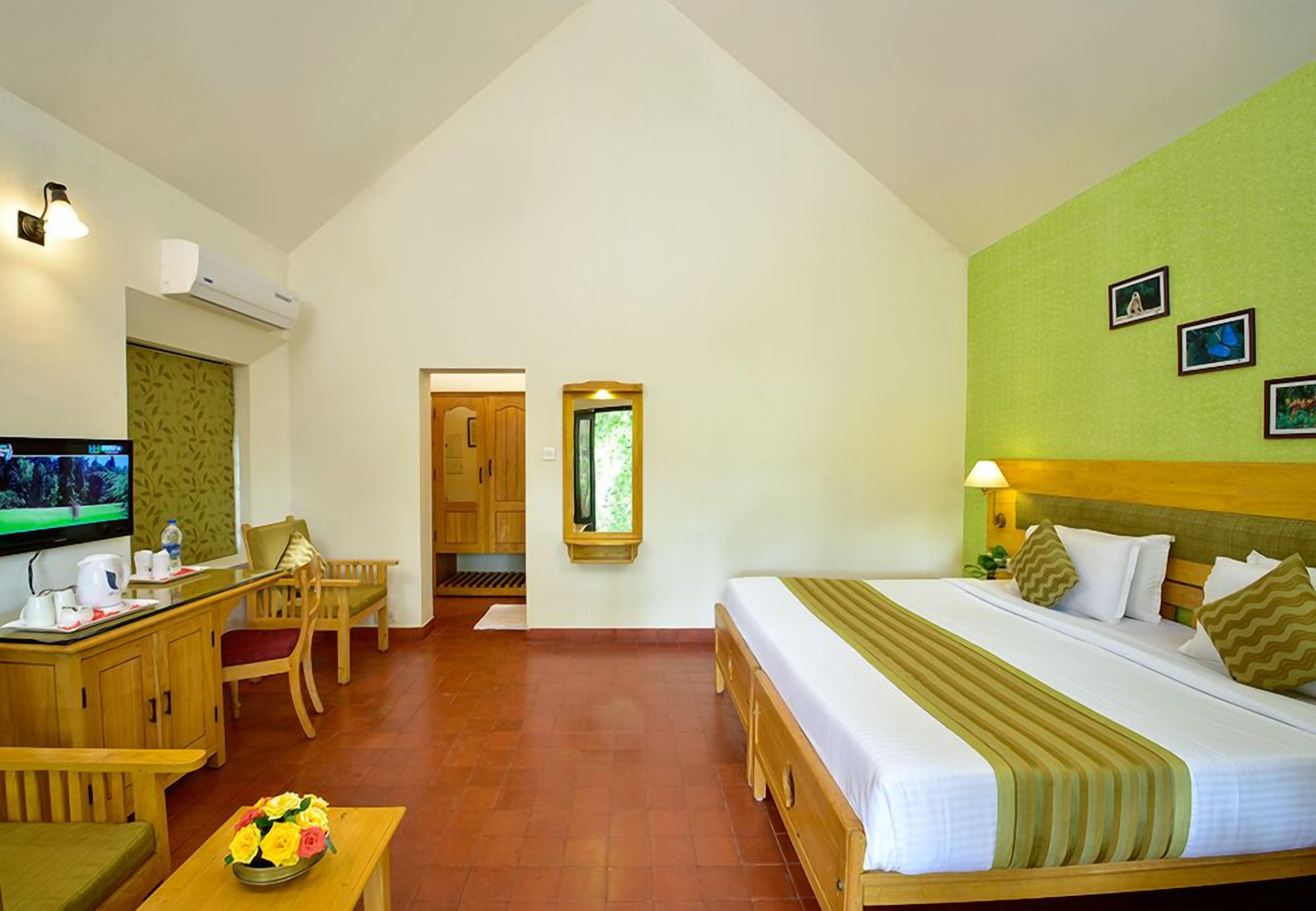 A hotel room with a bed, a desk with a TV, a chair, and a small table with flowers.