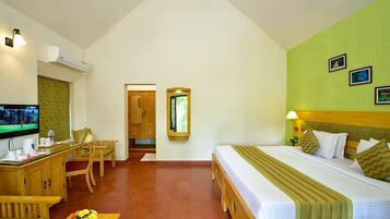 A hotel room with a bed, a desk with a TV, a chair, and a small table with flowers.