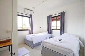 Ein Zimmer mit zwei Einzelbetten, einem Schreibtisch mit Stuhl, einer Klimaanlage und einem Fenster mit Vorhängen.